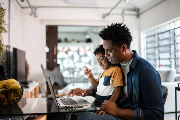 Father working on a laptop with his young child at home